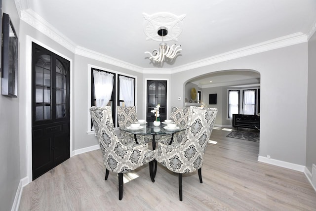 dining space with ornamental molding, light wood-type flooring, arched walkways, and a chandelier