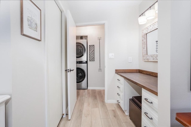 clothes washing area with light wood finished floors, laundry area, stacked washing maching and dryer, and baseboards