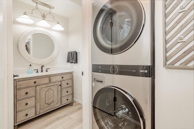 clothes washing area featuring laundry area, light wood-type flooring, stacked washer / drying machine, and a sink