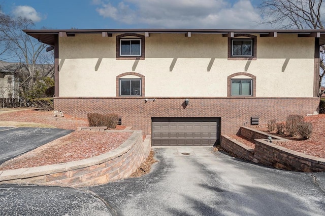 view of front facade featuring brick siding, stucco siding, an attached garage, and aphalt driveway