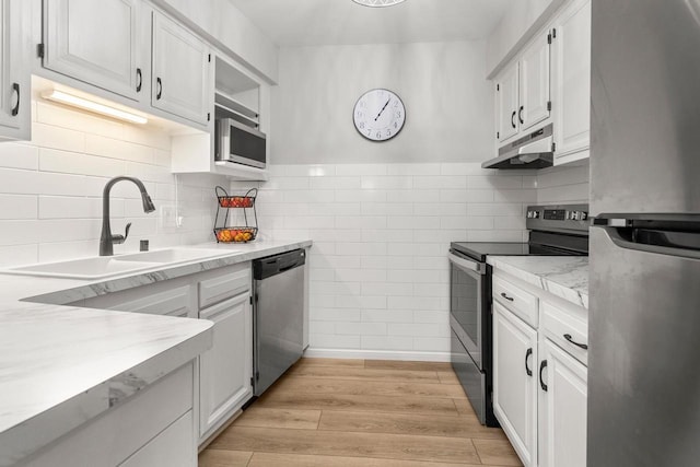 kitchen with under cabinet range hood, light wood-type flooring, white cabinets, stainless steel appliances, and a sink