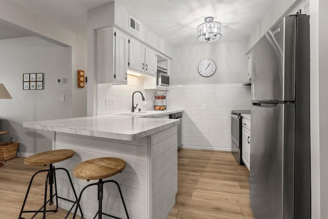 kitchen with visible vents, light wood-style flooring, a sink, stainless steel appliances, and a peninsula