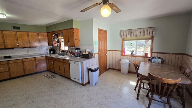 kitchen with dishwasher, light floors, brown cabinets, and wainscoting