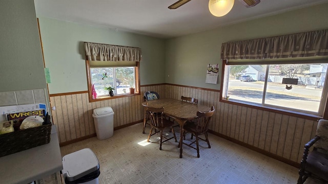 dining space with a ceiling fan, light floors, wood walls, and wainscoting