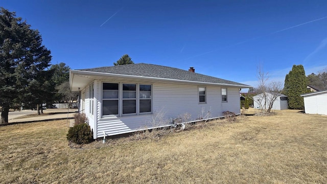 back of house with an outbuilding, a chimney, a shingled roof, and a yard