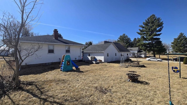 back of property with an outdoor fire pit, a lawn, and a chimney