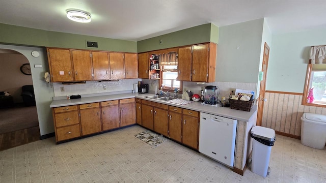 kitchen with brown cabinets, wainscoting, white dishwasher, light floors, and light countertops