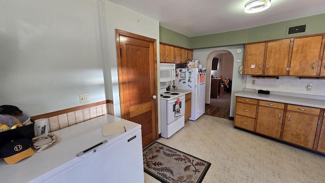 kitchen featuring arched walkways, visible vents, white appliances, and brown cabinetry