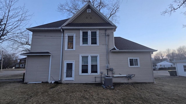 back of house featuring central air condition unit, a shingled roof, and a yard