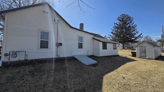 rear view of house featuring a lawn, a storage unit, and an outdoor structure