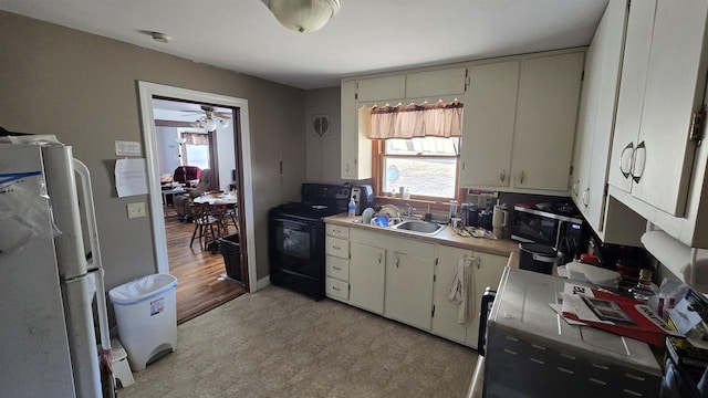 kitchen with ceiling fan, light floors, freestanding refrigerator, black electric range oven, and a sink