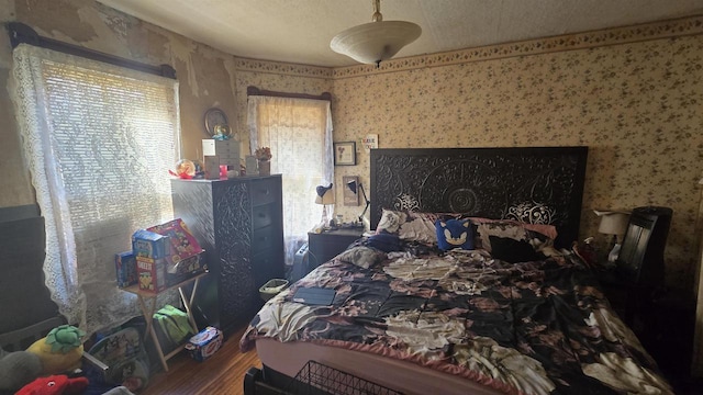 bedroom with wallpapered walls, wood finished floors, and a textured ceiling