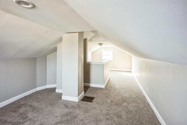 additional living space with visible vents, baseboards, carpet flooring, and vaulted ceiling