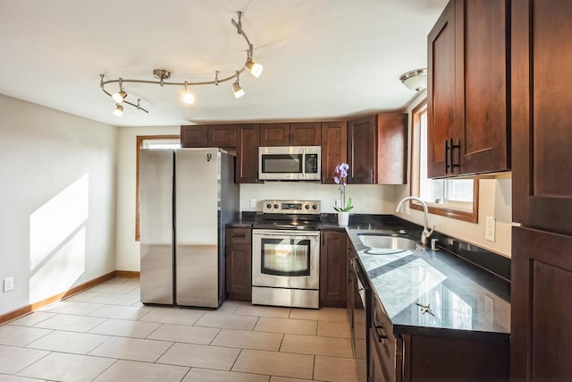 kitchen with a sink, stainless steel appliances, dark stone counters, light tile patterned flooring, and baseboards