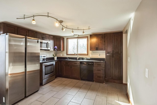 kitchen featuring baseboards, a sink, rail lighting, appliances with stainless steel finishes, and dark countertops