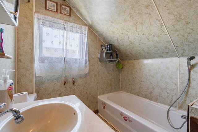 full bath with a sink, a tub, and vaulted ceiling