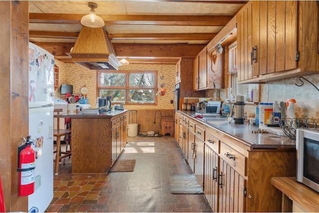 kitchen with stainless steel microwave, beamed ceiling, brown cabinetry, and stone finish flooring