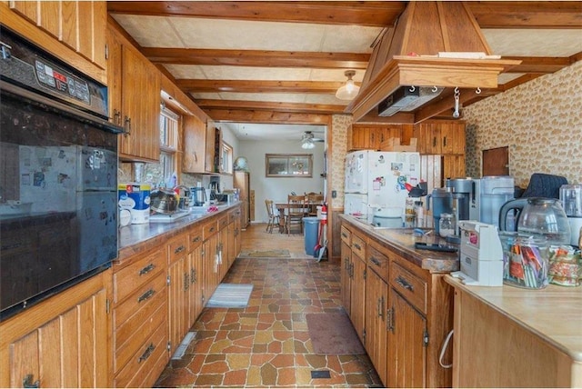 kitchen with brown cabinetry, freestanding refrigerator, oven, ceiling fan, and stone finish floor