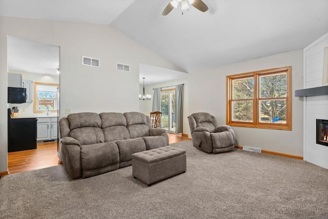 living area featuring a glass covered fireplace, ceiling fan with notable chandelier, and visible vents