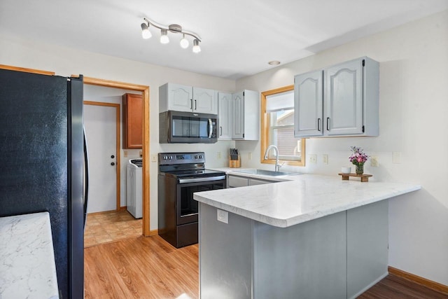 kitchen with a peninsula, freestanding refrigerator, a sink, range with electric cooktop, and light countertops