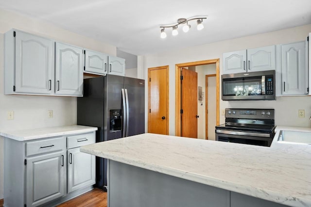 kitchen with a sink, stainless steel appliances, a peninsula, and gray cabinets