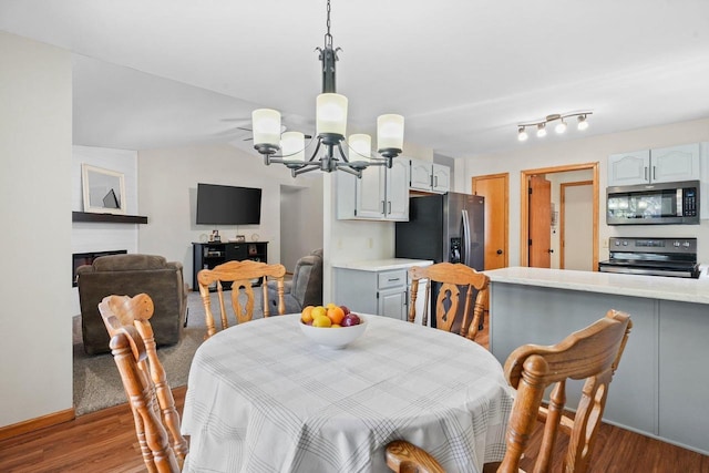 dining area featuring a fireplace, an inviting chandelier, wood finished floors, and vaulted ceiling