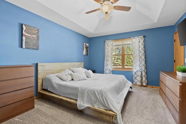 carpeted bedroom featuring a tray ceiling, baseboards, and ceiling fan