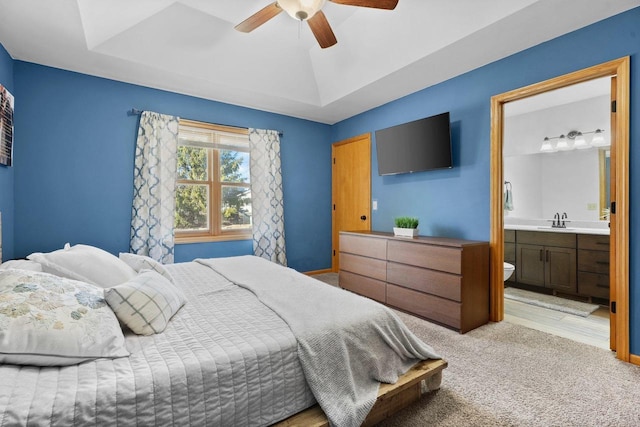 bedroom with a ceiling fan, a sink, ensuite bath, a raised ceiling, and light colored carpet