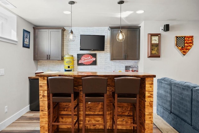 bar featuring light wood finished floors, backsplash, baseboards, bar, and hanging light fixtures