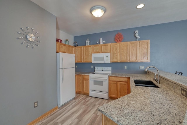 kitchen with light stone counters, a peninsula, light wood-style floors, white appliances, and a sink