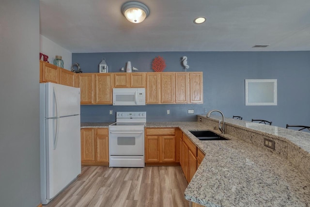 kitchen featuring light stone counters, a peninsula, light wood-style floors, white appliances, and a sink