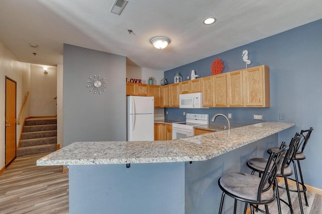 kitchen featuring white appliances, light wood finished floors, a peninsula, light brown cabinetry, and a kitchen breakfast bar