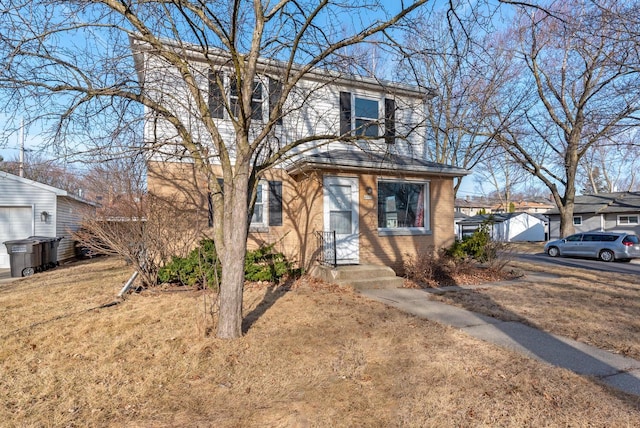 view of front facade with a front yard, an outbuilding, and brick siding