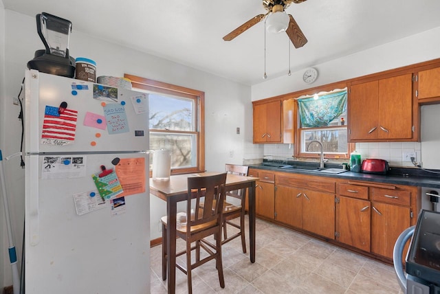 kitchen featuring brown cabinetry, plenty of natural light, freestanding refrigerator, ceiling fan, and a sink