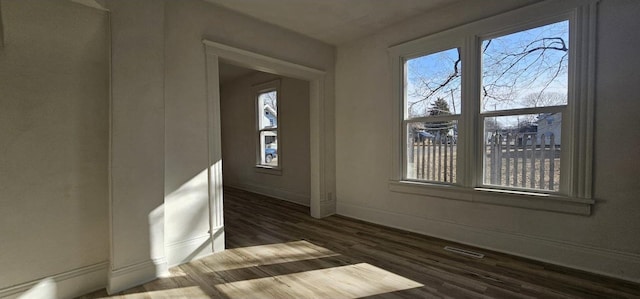 empty room featuring dark wood finished floors, visible vents, and baseboards