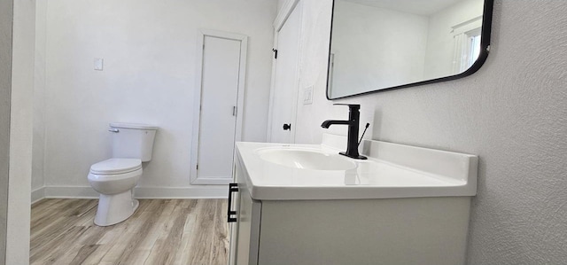 half bath featuring toilet, vanity, baseboards, and wood finished floors