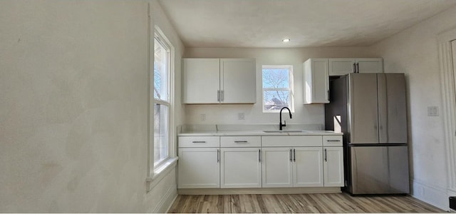 kitchen featuring light wood finished floors, freestanding refrigerator, a sink, light countertops, and white cabinets