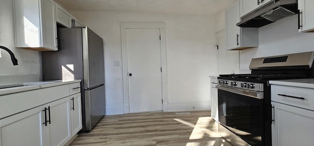 kitchen with light wood-style flooring, under cabinet range hood, a sink, stainless steel appliances, and light countertops