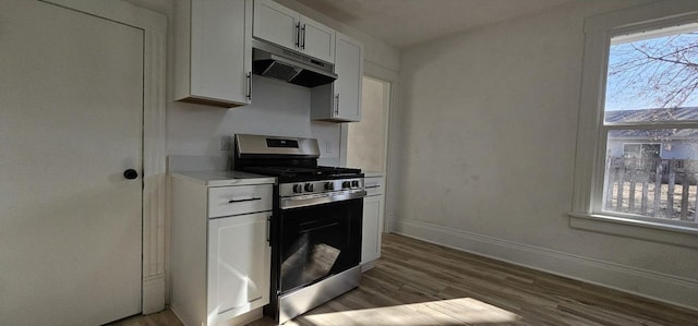 kitchen featuring baseboards, light countertops, white cabinets, under cabinet range hood, and gas range