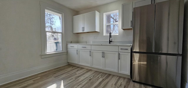 kitchen with light countertops, light wood finished floors, freestanding refrigerator, and a sink