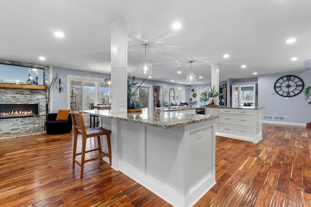 kitchen with visible vents, a sink, a stone fireplace, white cabinets, and light stone countertops