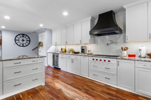 kitchen featuring cooktop, dark wood-type flooring, custom range hood, wine cooler, and backsplash