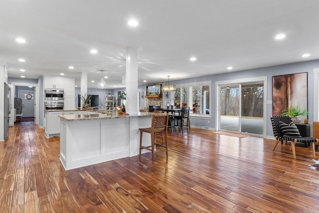 kitchen with light stone counters, wood finished floors, recessed lighting, white cabinets, and a large island with sink