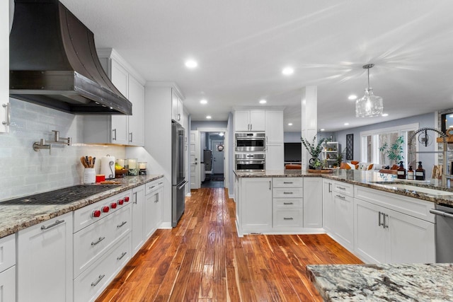 kitchen featuring premium range hood, appliances with stainless steel finishes, wood finished floors, white cabinetry, and a sink