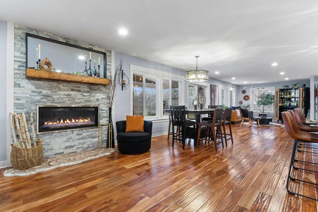 dining area with a notable chandelier, wood finished floors, recessed lighting, a stone fireplace, and baseboards