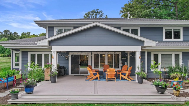 rear view of property featuring an outdoor fire pit, roof with shingles, and a wooden deck