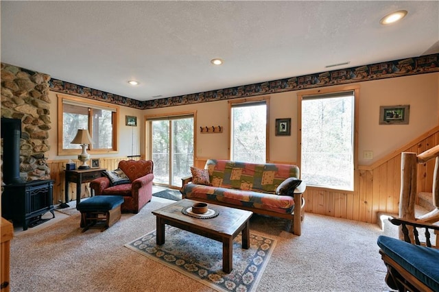 carpeted living room featuring a wainscoted wall, a textured ceiling, recessed lighting, wood walls, and a wood stove