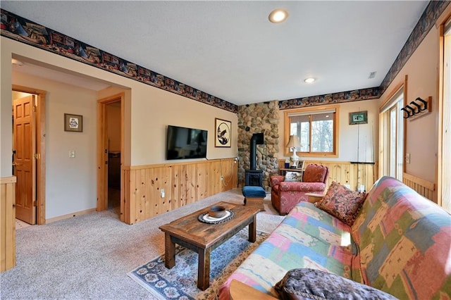 living area with a wood stove, wooden walls, carpet, and wainscoting