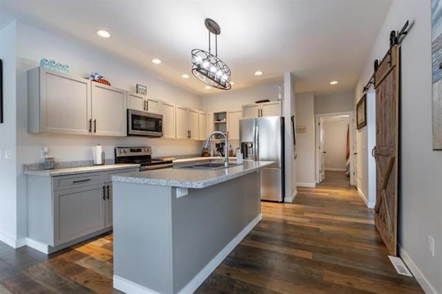 kitchen featuring gray cabinetry, dark wood finished floors, a barn door, appliances with stainless steel finishes, and a sink