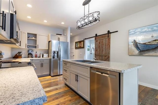 kitchen with light wood finished floors, a center island with sink, a barn door, stainless steel appliances, and a sink